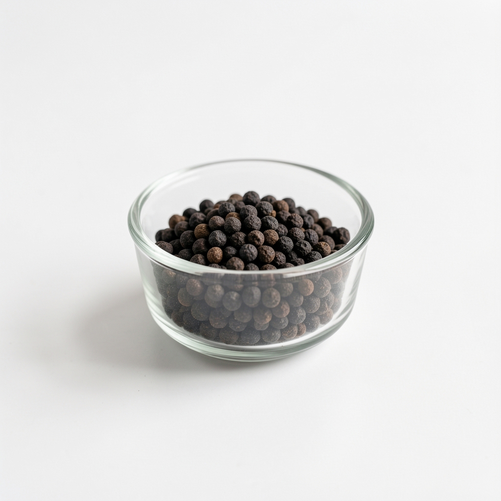Small glass measuring dish with dark-toned supplement granules on clean white surface, product research context